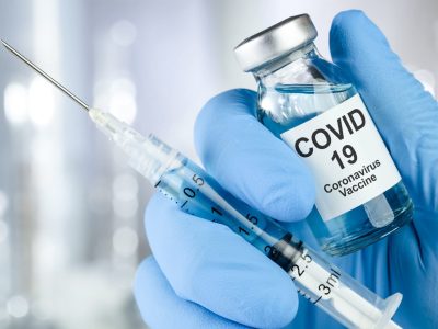 Healthcare cure concept with a hand in blue medical gloves holding Coronavirus, Covid 19 virus, vaccine vial