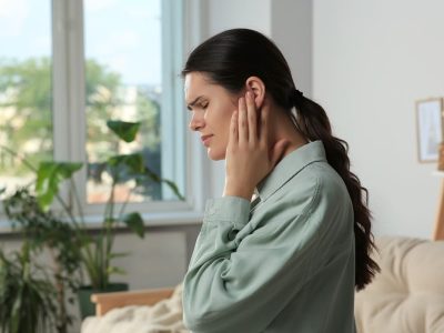 Young woman suffering from ear pain at home