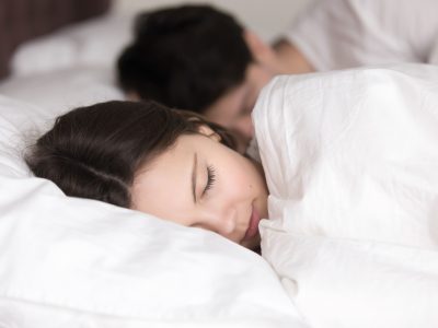 Couple having a restful sleep, young pretty lady lying on pillow under covering in comfortable white bed, looking peaceful and serene, soft healthy sleep on weekend and good dreams