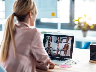 Back view of female employee speaking on video call with diverse colleagues on online briefing with laptop at home.